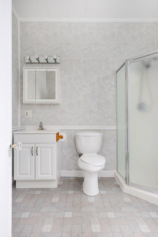 bathroom featuring an enclosed shower, ornamental molding, vanity, and toilet