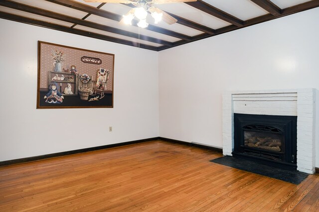 unfurnished living room featuring beamed ceiling, wood-type flooring, a brick fireplace, and ceiling fan