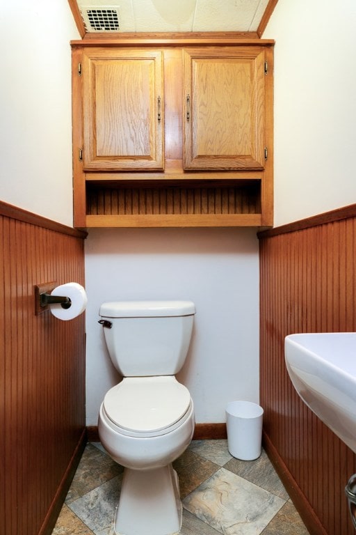 bathroom featuring toilet and wood walls