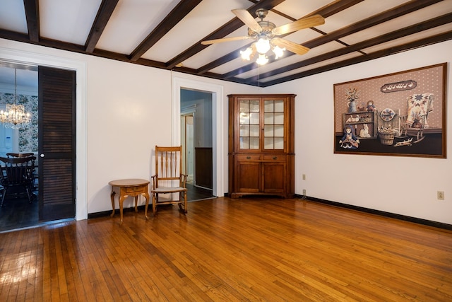 living area featuring dark wood-type flooring, ceiling fan with notable chandelier, and beamed ceiling