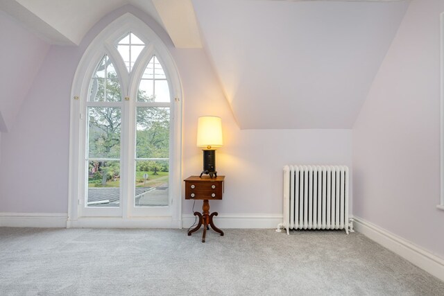 interior space with lofted ceiling, radiator heating unit, and light carpet