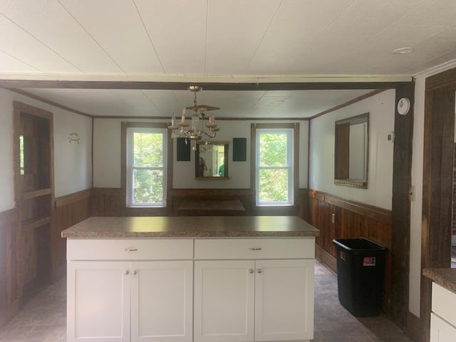 kitchen featuring an inviting chandelier, a wealth of natural light, wooden walls, and white cabinets