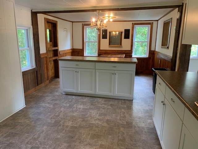 kitchen with a notable chandelier, ornamental molding, wooden walls, and white cabinets