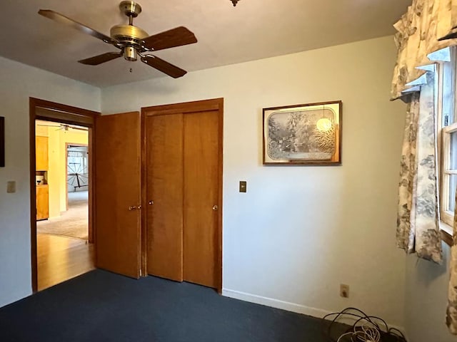 unfurnished bedroom with dark colored carpet, ceiling fan, and a closet