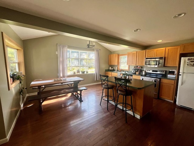 kitchen featuring a kitchen bar, lofted ceiling with beams, appliances with stainless steel finishes, dark hardwood / wood-style flooring, and a kitchen island