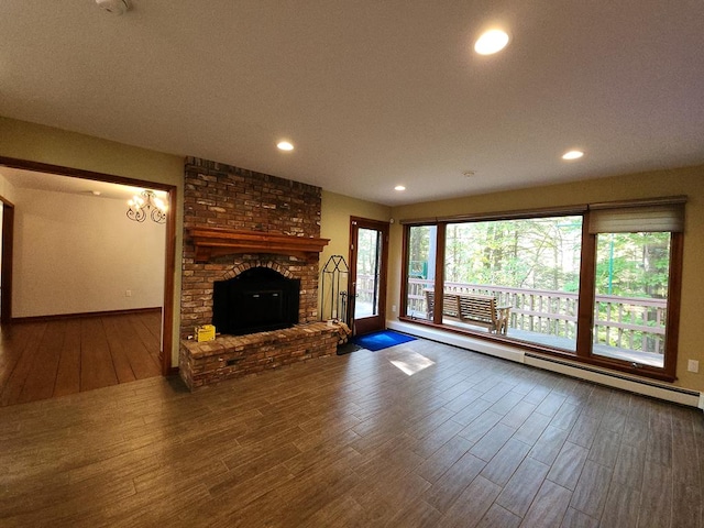 unfurnished living room featuring a notable chandelier, a fireplace, wood-type flooring, and a baseboard heating unit