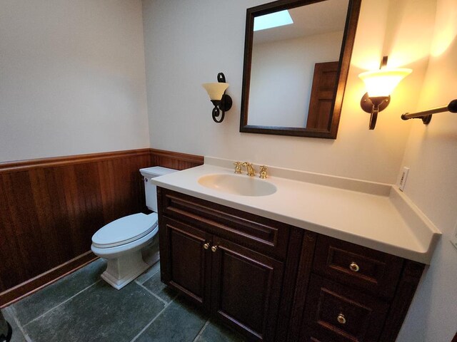 bathroom featuring vanity, toilet, and wood walls