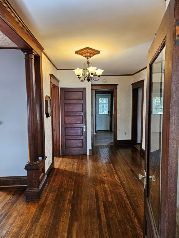 hall with ornate columns, crown molding, dark wood-type flooring, and an inviting chandelier