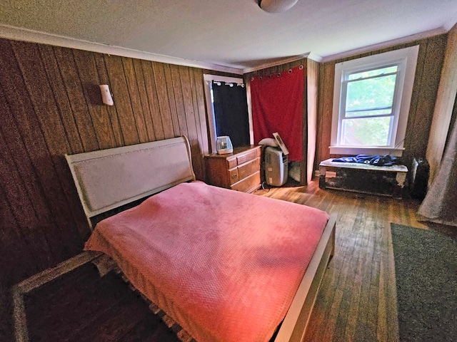 bedroom with crown molding, wooden walls, and dark wood-type flooring