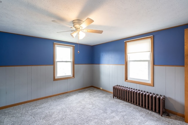 carpeted empty room with ceiling fan, radiator heating unit, and a textured ceiling