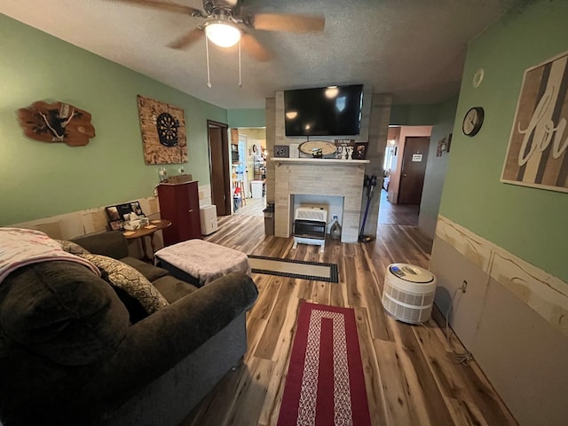 living room featuring ceiling fan, a brick fireplace, hardwood / wood-style floors, and a textured ceiling