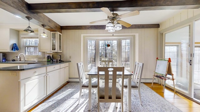 dining room with sink, light hardwood / wood-style flooring, ceiling fan, beam ceiling, and wood walls