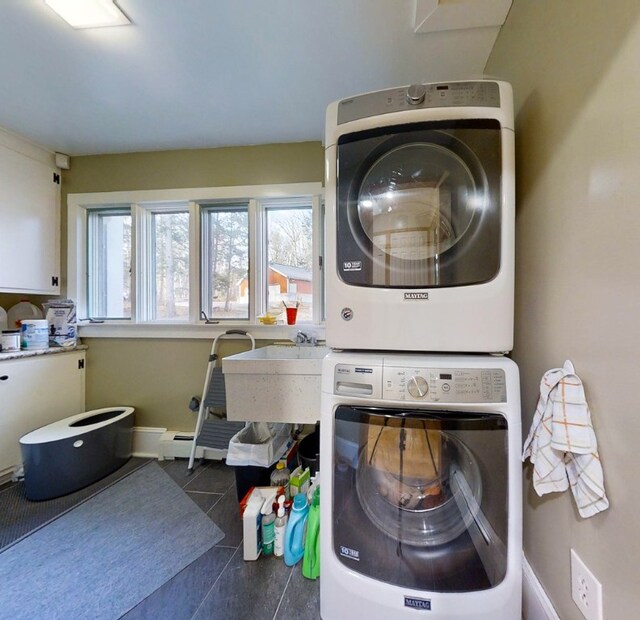 washroom featuring stacked washing maching and dryer, a baseboard heating unit, and dark tile patterned flooring