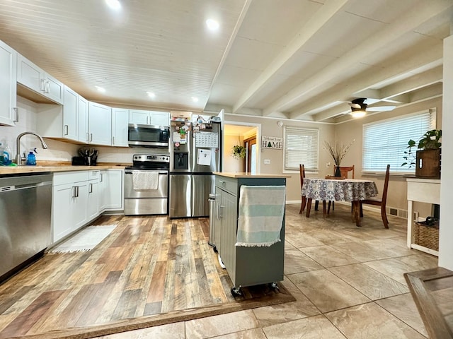 kitchen featuring beam ceiling, sink, stainless steel appliances, and white cabinetry