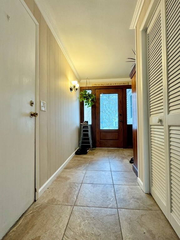 doorway featuring ornamental molding and wood walls