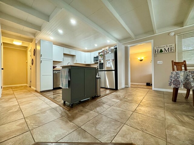 kitchen with light tile patterned flooring, a kitchen island, appliances with stainless steel finishes, white cabinetry, and beam ceiling