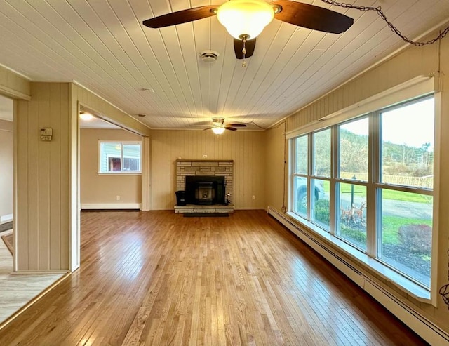 unfurnished living room featuring hardwood / wood-style flooring, ceiling fan, baseboard heating, a wealth of natural light, and a stone fireplace