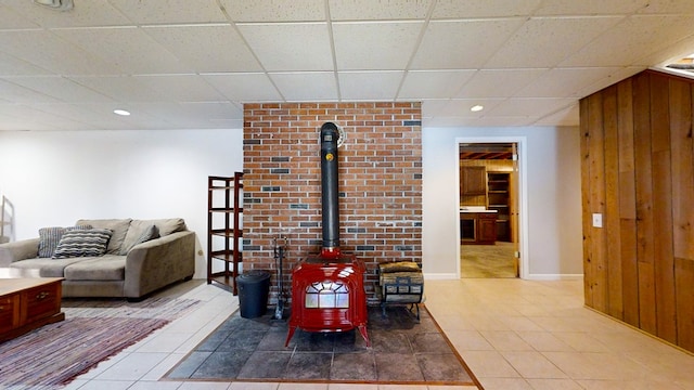 living room featuring tile patterned flooring, a wood stove, a drop ceiling, and wood walls