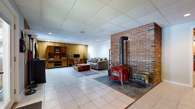 living room featuring a wood stove, light tile patterned floors, and a drop ceiling