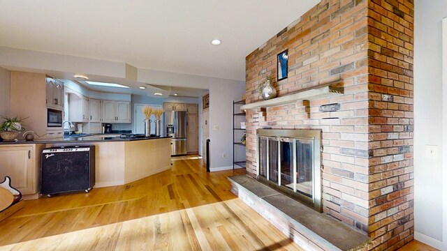 kitchen with built in microwave, sink, light hardwood / wood-style floors, stainless steel refrigerator with ice dispenser, and a brick fireplace