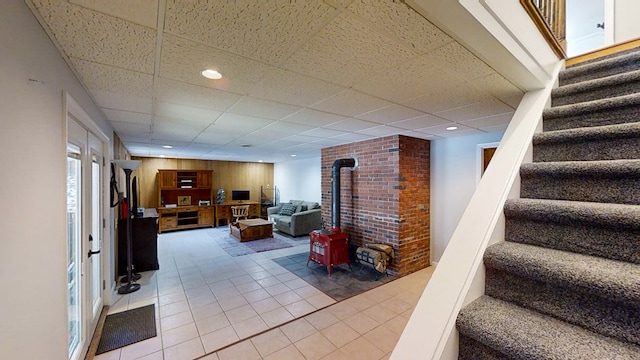 interior space with tile patterned flooring, a wood stove, and a drop ceiling