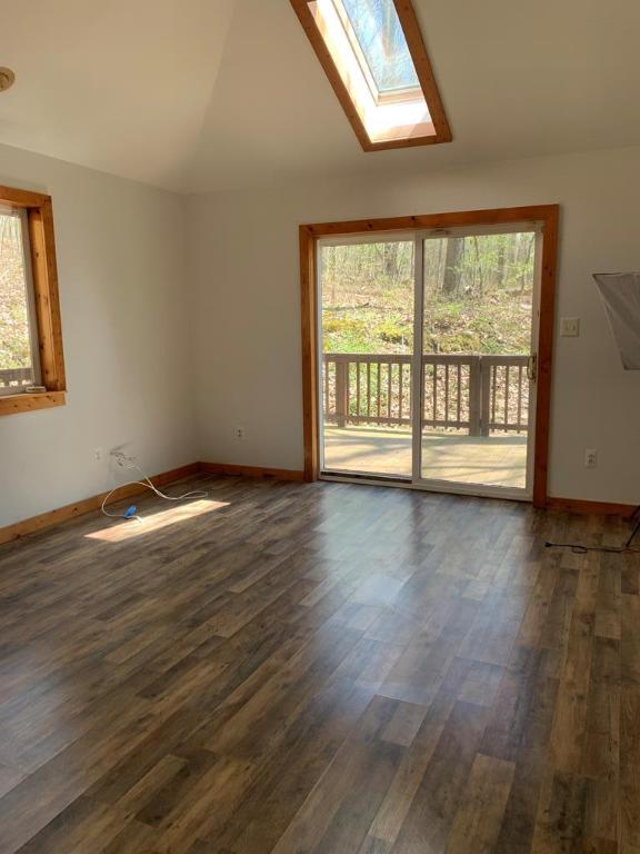 unfurnished living room with dark hardwood / wood-style floors, plenty of natural light, and vaulted ceiling with skylight