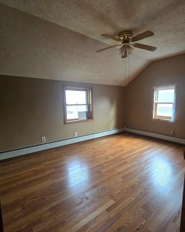 additional living space with lofted ceiling, hardwood / wood-style floors, a textured ceiling, and a healthy amount of sunlight