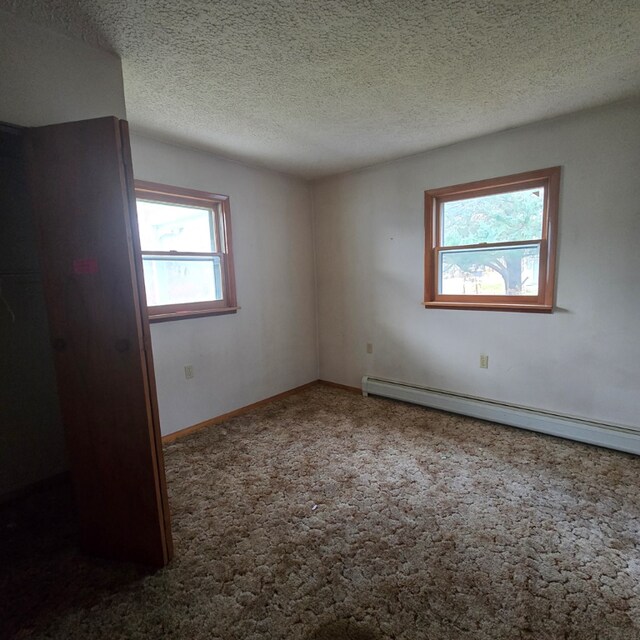 empty room featuring a baseboard radiator, a healthy amount of sunlight, a textured ceiling, and carpet flooring