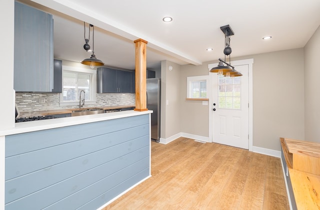 kitchen with appliances with stainless steel finishes, pendant lighting, sink, decorative backsplash, and light wood-type flooring