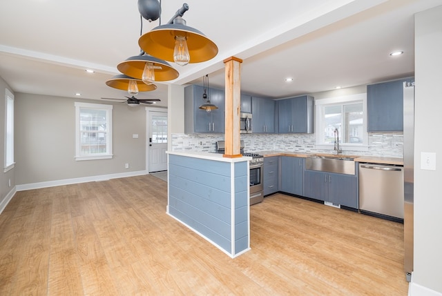 kitchen featuring sink, hanging light fixtures, kitchen peninsula, stainless steel appliances, and light hardwood / wood-style floors