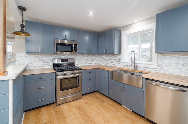 kitchen with hanging light fixtures, blue cabinetry, sink, and appliances with stainless steel finishes