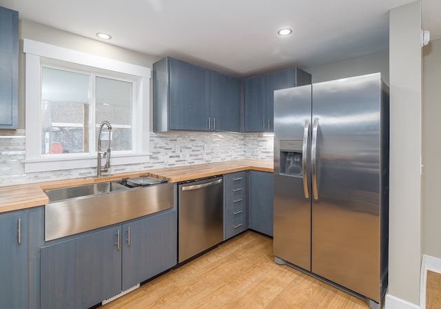 kitchen with appliances with stainless steel finishes, sink, wooden counters, and blue cabinetry