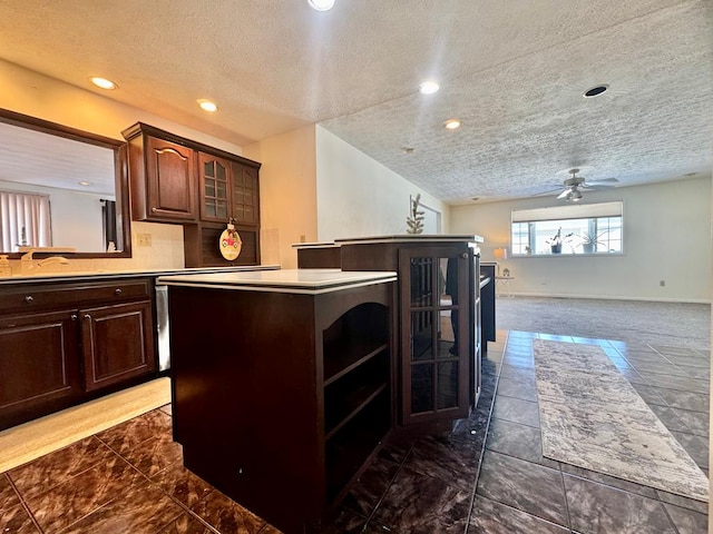 kitchen with a kitchen island, sink, dark brown cabinetry, ceiling fan, and a textured ceiling