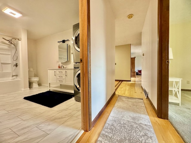 full bathroom featuring stacked washer / drying machine, wood-type flooring, bathing tub / shower combination, and toilet