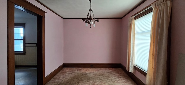 carpeted empty room featuring ornamental molding, plenty of natural light, and an inviting chandelier