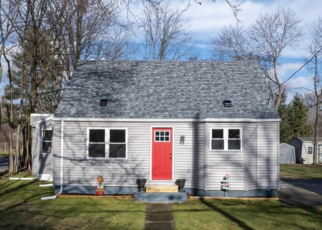 cape cod house with a front lawn and a storage unit