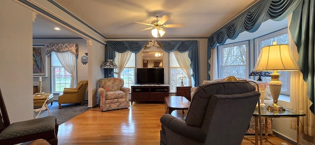 living room with wood-type flooring, ornamental molding, and ceiling fan