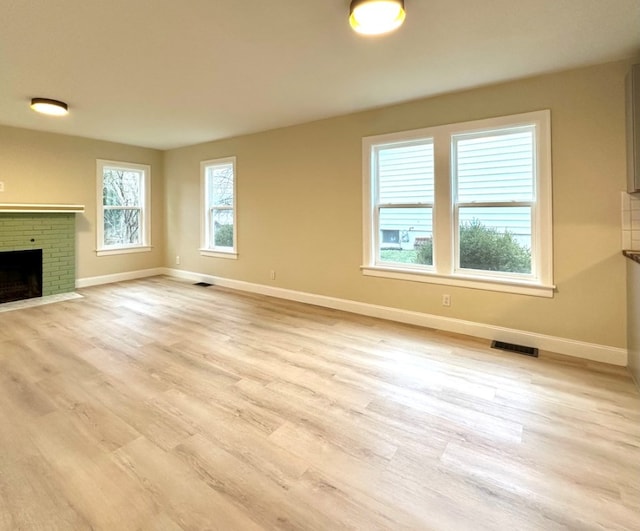 unfurnished living room with light hardwood / wood-style floors and a brick fireplace