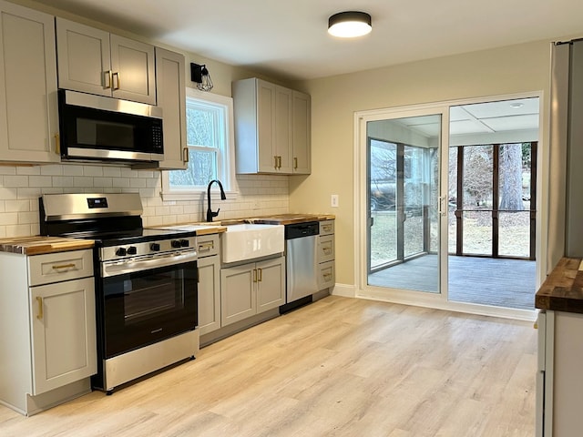 kitchen with appliances with stainless steel finishes, butcher block counters, sink, and light wood-type flooring