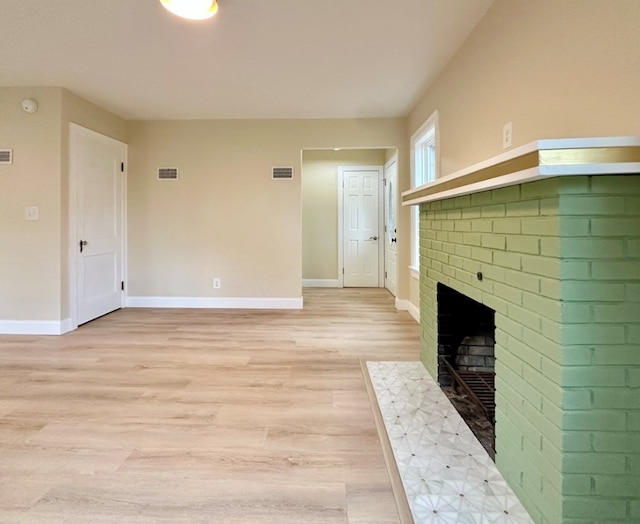 unfurnished living room with a brick fireplace and light wood-type flooring