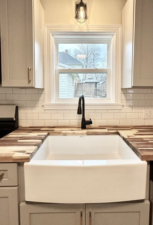 interior details featuring tasteful backsplash, white cabinetry, butcher block counters, and sink