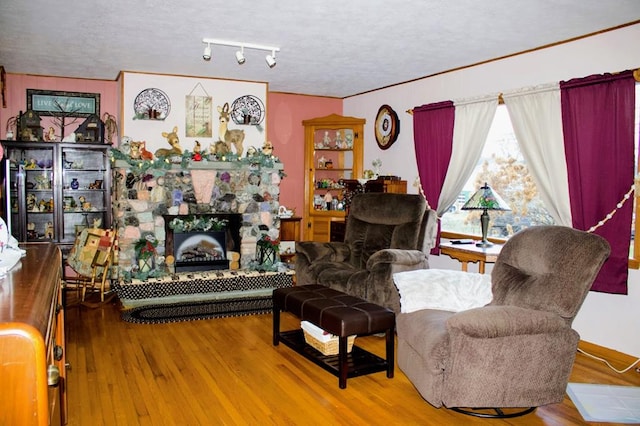 living room featuring crown molding, hardwood / wood-style flooring, a stone fireplace, and a textured ceiling