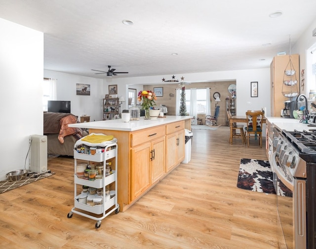 kitchen with sink, radiator heating unit, stainless steel gas range oven, light wood-type flooring, and light brown cabinets