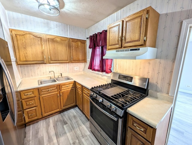 kitchen with stainless steel appliances, sink, a textured ceiling, and light hardwood / wood-style floors