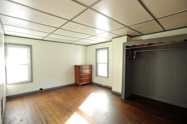 unfurnished bedroom with multiple windows, hardwood / wood-style flooring, a paneled ceiling, and a closet