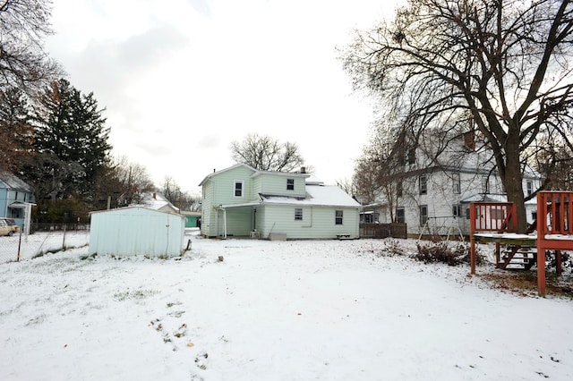 snow covered rear of property with a shed and a wooden deck