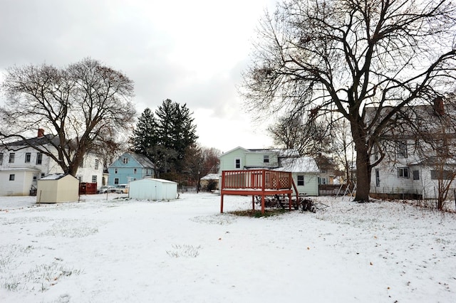 snowy yard with a wooden deck and a storage unit