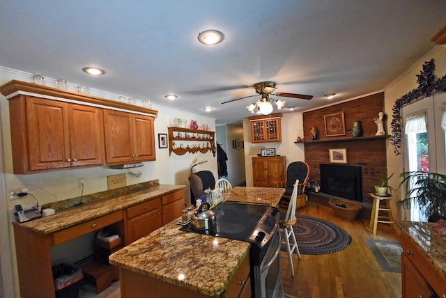 kitchen with stainless steel electric range, dark hardwood / wood-style floors, a center island, light stone countertops, and a brick fireplace