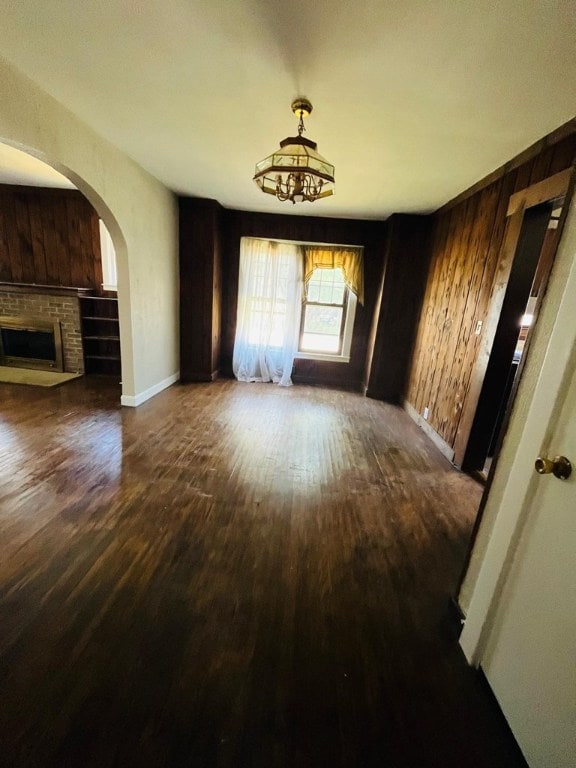 unfurnished living room featuring dark wood-type flooring, wooden walls, and a brick fireplace