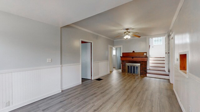 unfurnished living room featuring crown molding, ceiling fan, a fireplace, and light hardwood / wood-style floors